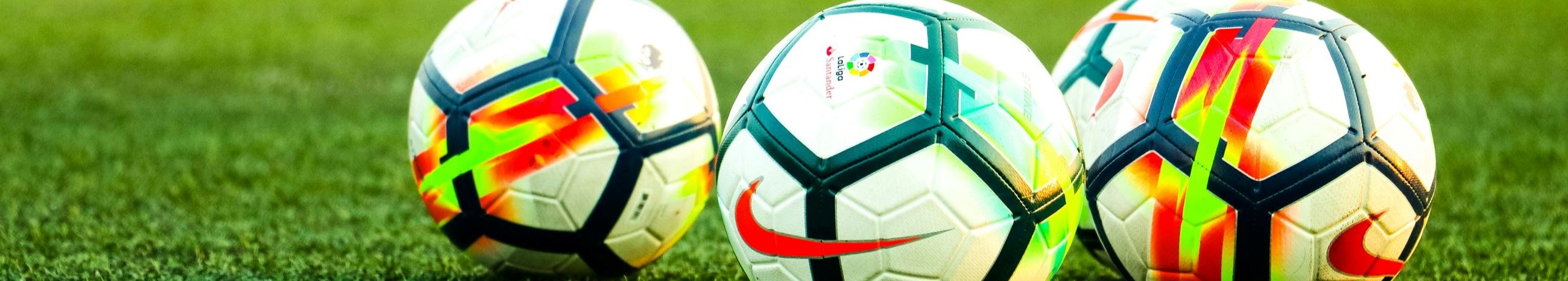 Four Nike soccer balls in a field at sunset